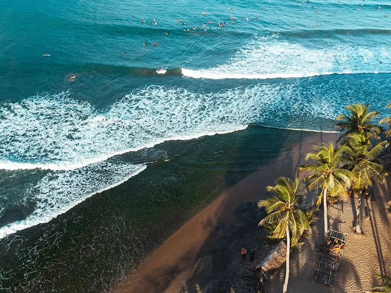 Aerial view of Arugam Bay's famous Main Point surf break, showing powerful waves and numerous surfers in the ocean, highlighting the popular surfing scene as a primary things to do in Arugam Bay attraction.