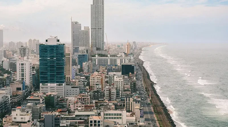 An aerial view of the modern Colombo city skyline, high-rise buildings, and the railway line running along the ocean, showcasing things to do in Colombo.