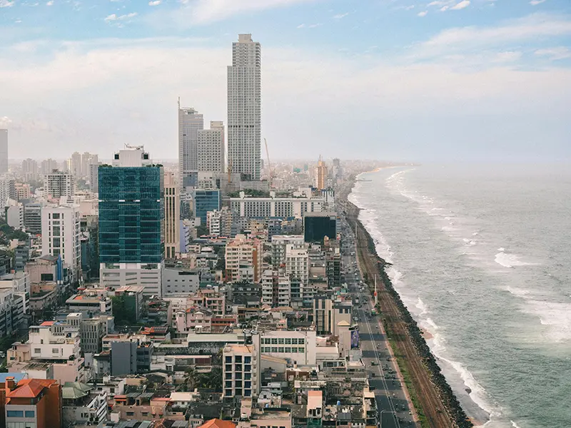 An aerial view of the modern Colombo city skyline, high-rise buildings, and the railway line running along the ocean, showcasing things to do in Colombo.