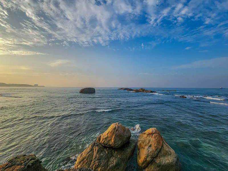 A wide view of the Indian Ocean with large rocks in the foreground and a fading sunset sky, captured from the ramparts when exploring things to do in Galle Fort.