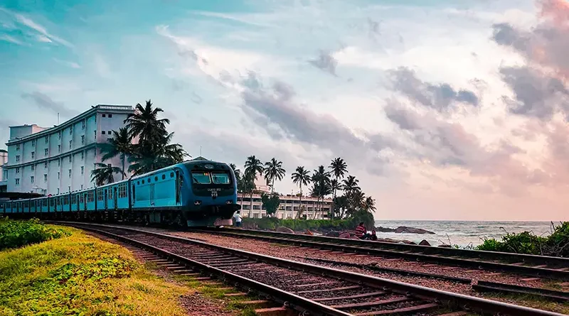 A blue train travels along the coastal railway track beside the Indian Ocean, illustrating one of the best ways of getting around Sri Lanka.