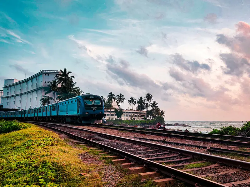 A blue train travels along the coastal railway track beside the Indian Ocean, illustrating one of the best ways of getting around Sri Lanka.