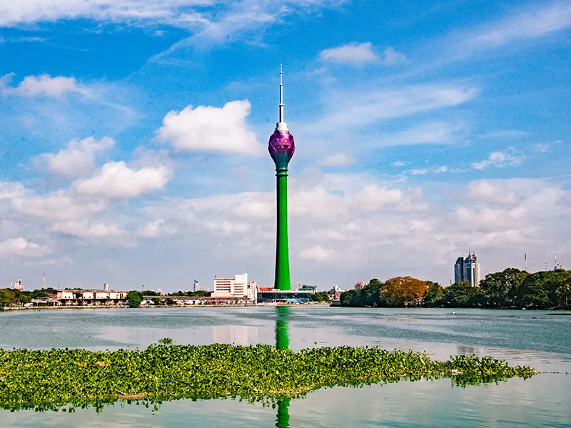 A scenic view of the futuristic Lotus Tower against a blue sky, reflecting in the water, a modern must-see among things to do in Colombo.