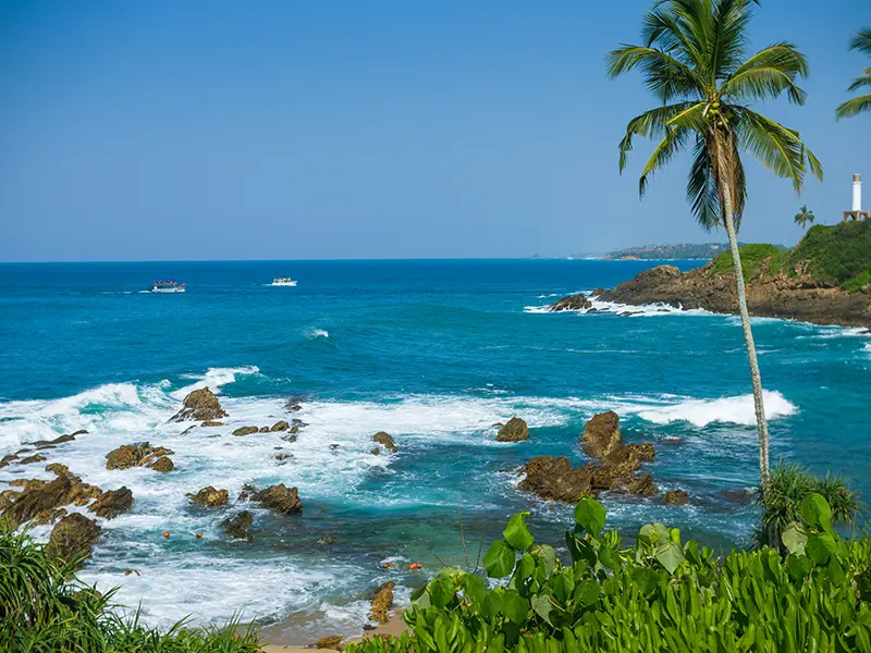 A secluded view of Secret Beach Mirissa, showing a small sandy cove, palm trees, and rocky outcrops meeting the clear blue ocean, a quiet spot for swimming and a key attraction for things to do in Mirissa.