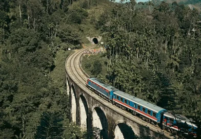 A blue and red train crossing the historic Nine Arch Bridge, one of the top things to do in Ella for photographers and travelers.