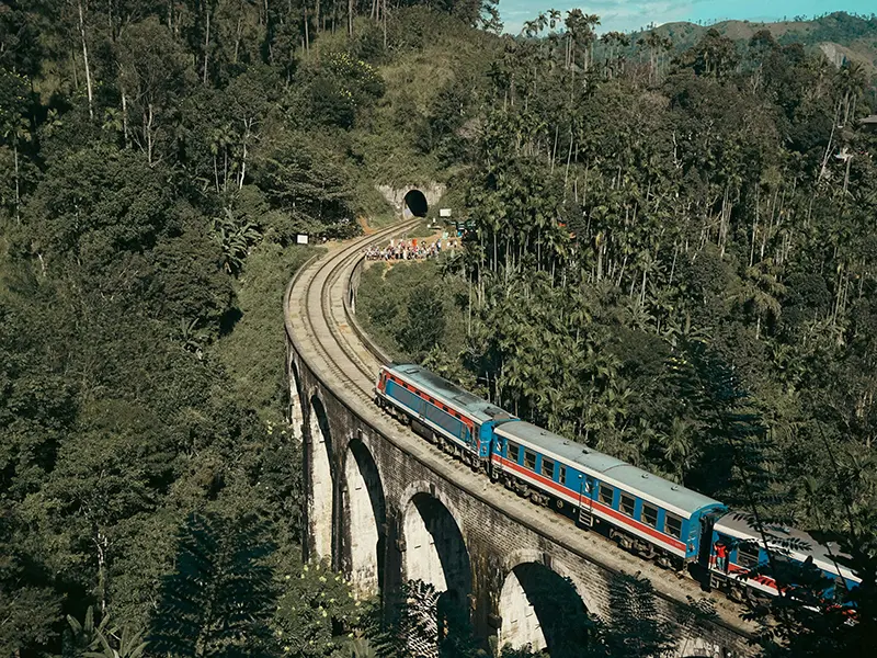 A blue and red train crossing the historic Nine Arch Bridge, one of the top things to do in Ella for photographers and travelers.