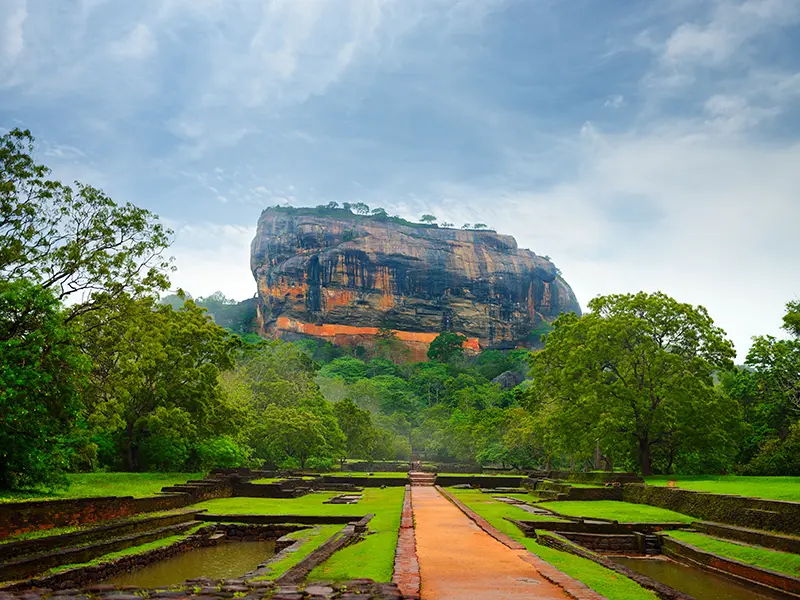 Tourists walk through the ancient brick and stone ruins of the meticulously planned Sigiriya Water Gardens, showcasing the grandeur of the lower palace complex and surrounding area.