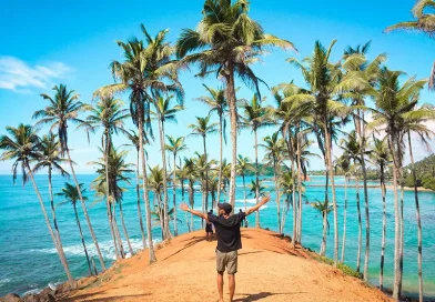 Things to do in Mirissa Sri Lanka: Traveler with arms wide open at the iconic Coconut Tree Hill viewpoint overlooking the turquoise ocean.