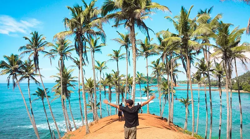 Things to do in Mirissa Sri Lanka: Traveler with arms wide open at the iconic Coconut Tree Hill viewpoint overlooking the turquoise ocean.