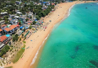 Aerial view of Unawatuna Beach, showing the vibrant crescent of golden sand, turquoise water, and the densely built-up shoreline of the main town, a popular destination for things to do in Unawatuna, Sri Lanka.