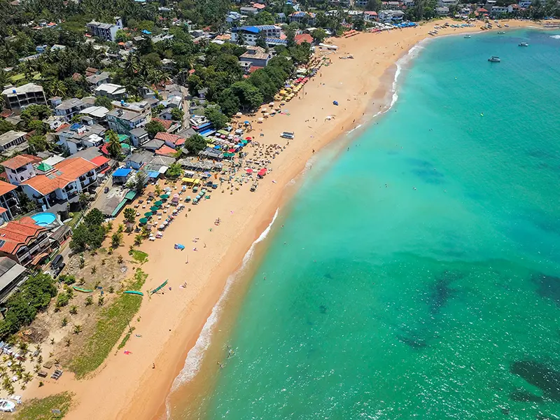 Aerial view of Unawatuna Beach, showing the vibrant crescent of golden sand, turquoise water, and the densely built-up shoreline of the main town, a popular destination for things to do in Unawatuna, Sri Lanka.