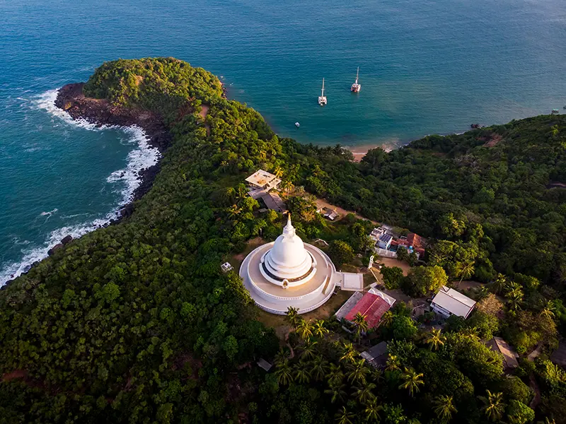 Aerial view of the serene white Japanese Peace Pagoda on Rumassala Hill, surrounded by lush jungle and overlooking the turquoise ocean, a spiritual and scenic highlight for things to do in Unawatuna.