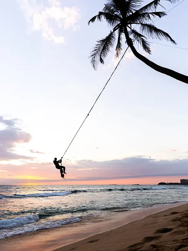 Silhouette of a person swinging from the famous palm tree rope swing at Wijaya Beach near Unawatuna at sunset, a hugely popular and photo-worthy experience among things to do in Unawatuna.